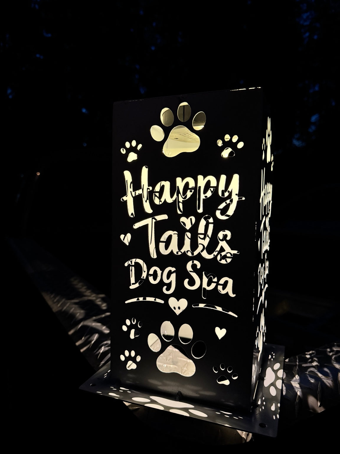 J Fab 6 by 12 inch Happy Tails Dog Spa luminary illuminated at night, close-up of lettering, hearts and paw prints